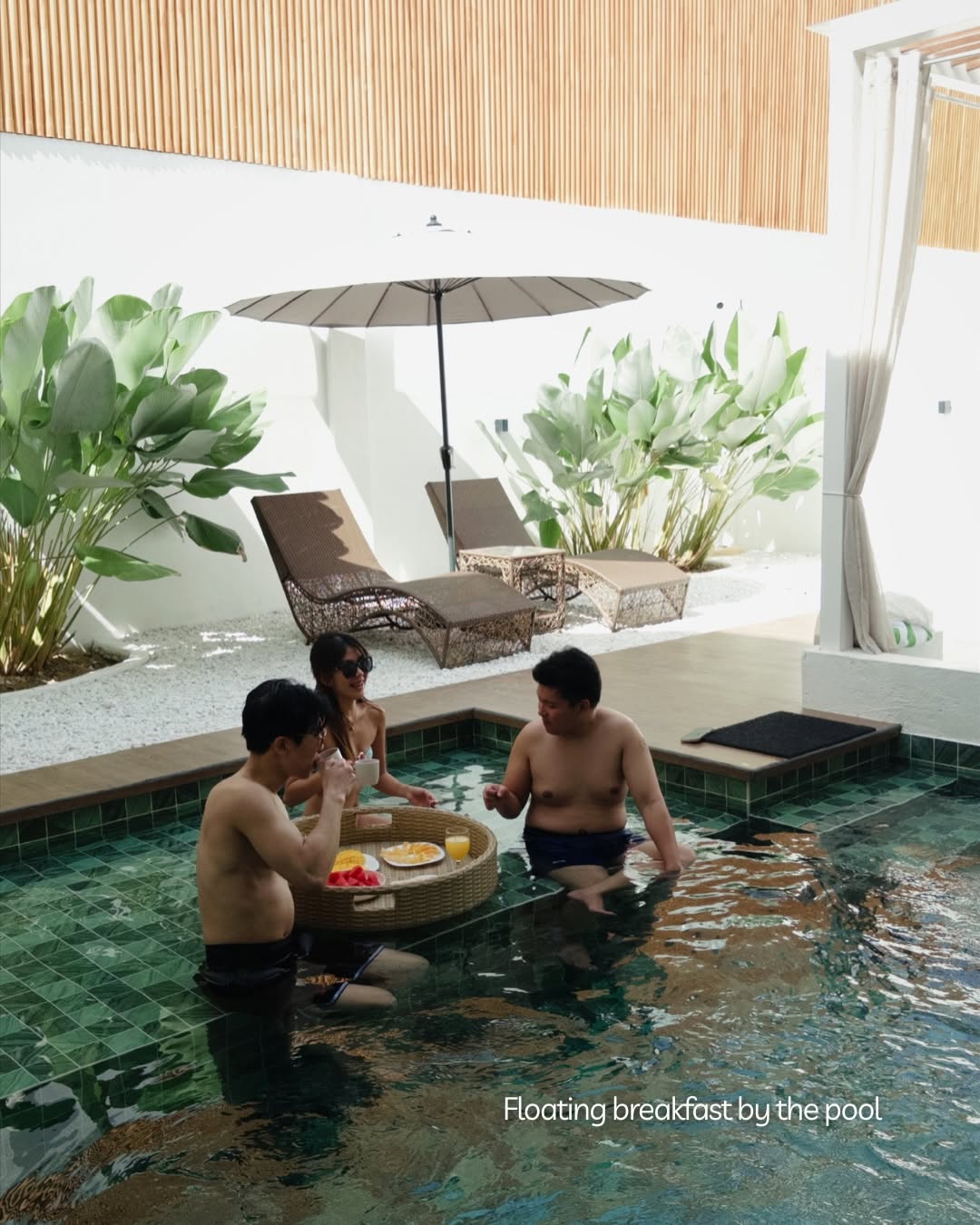 Three guests enjoying a floating breakfast tray with fruit and coffee in the private pool